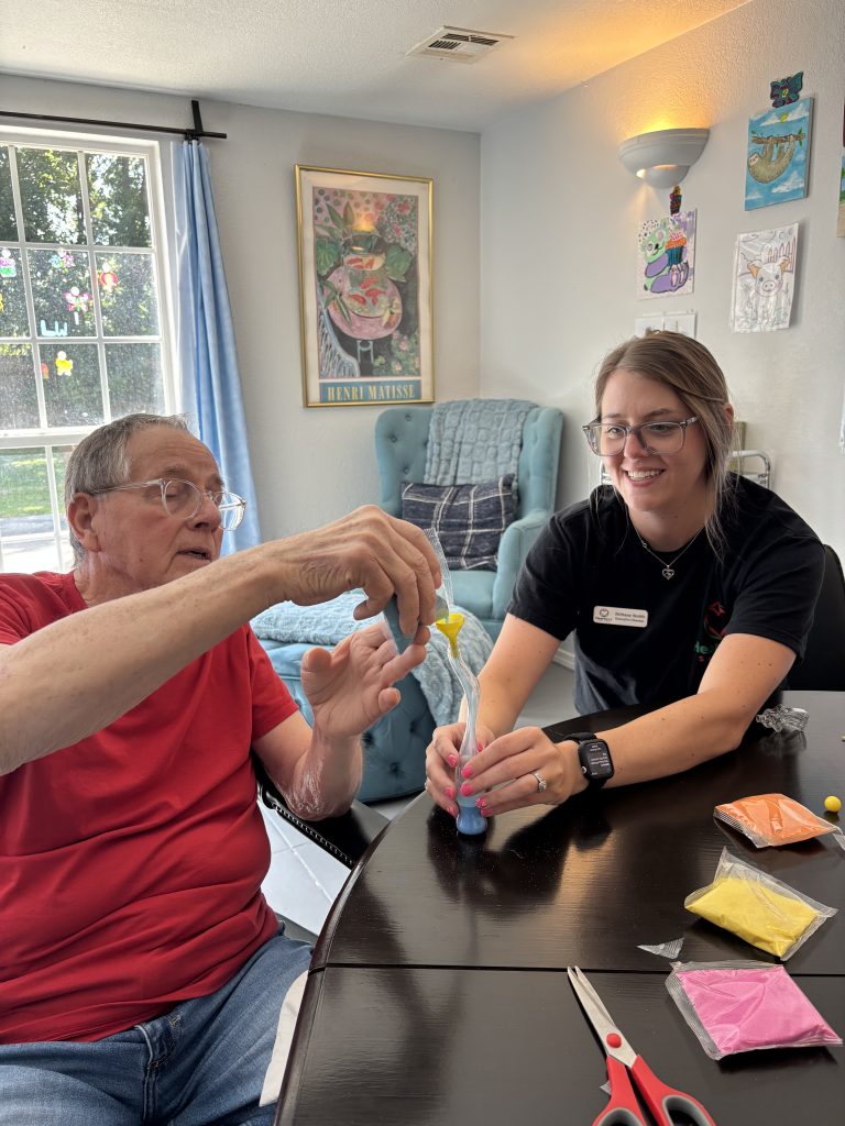 Executive Director of Heartland Suites Assisted Living in Oklahoma sitting with a senior resident and doing a craft together during a creative activity session.